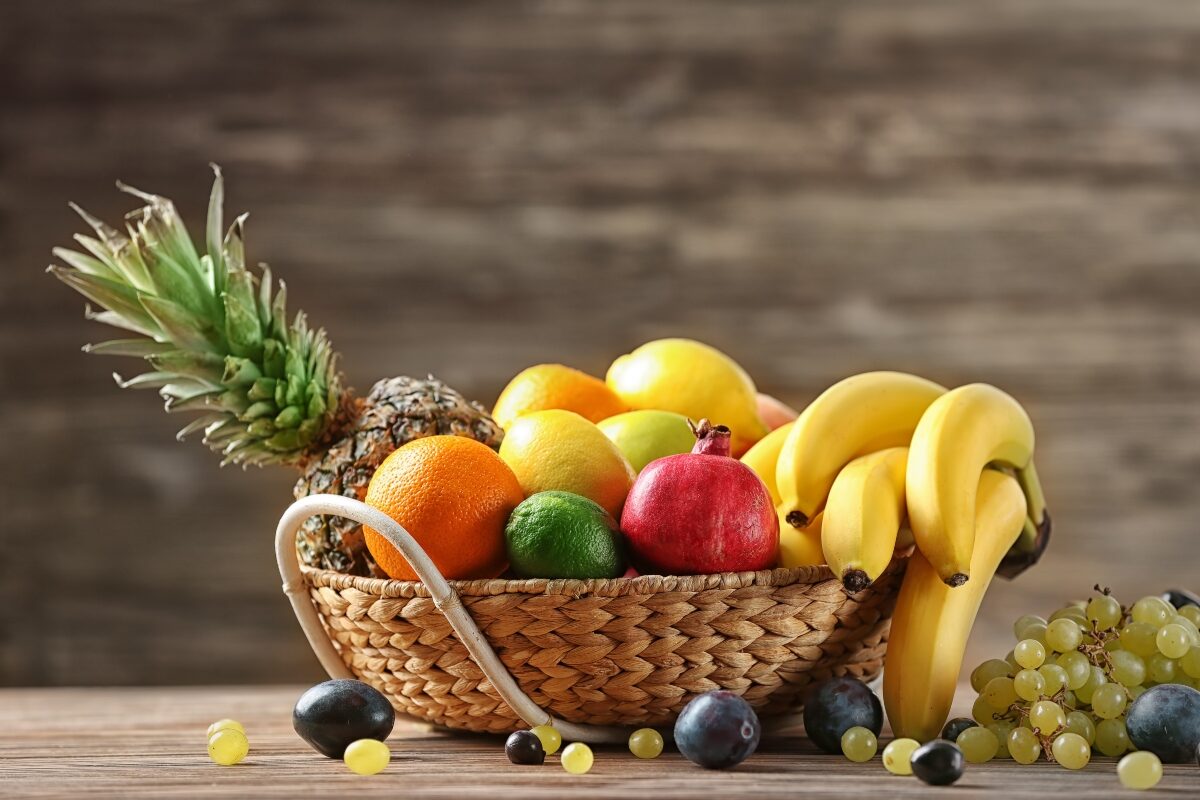 Un coș cu mai multe fructe: ananas, banane, avocado, citrice.