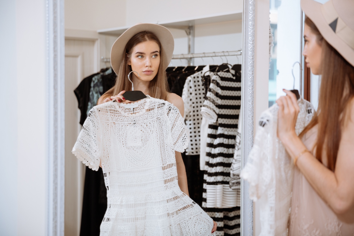 O femeie măsoară o rochie albă în fața oglinzii.