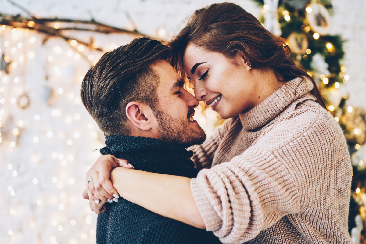 Un cuplu de îndrăgostiți se îmbrățișează. El poartă un pulover negru, ea un pulover bej.
