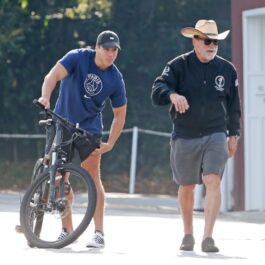 Arnold Schwarzenegger și Joseph Baena sunt îmbrăcați sport și se plimbă cu bicicletele