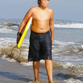 Joseph Baena la plajă cu o placă de surf în mână.