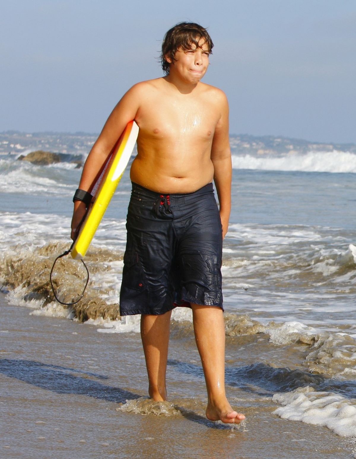Joseph Baena la plajă cu o placă de surf în mână.