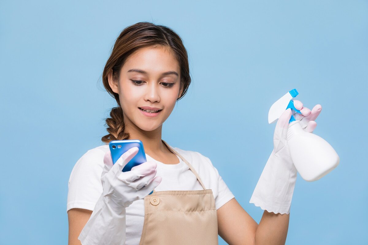 Femeie cu părul prins într-o coadă cu mănuși de curățenie care ține în timp ce studiază câteva metode de curățenie de pe internet