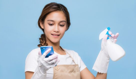 Femeie cu părul prins într-o coadă cu mănuși de curățenie care ține în timp ce studiază câteva metode de curățenie de pe internet
