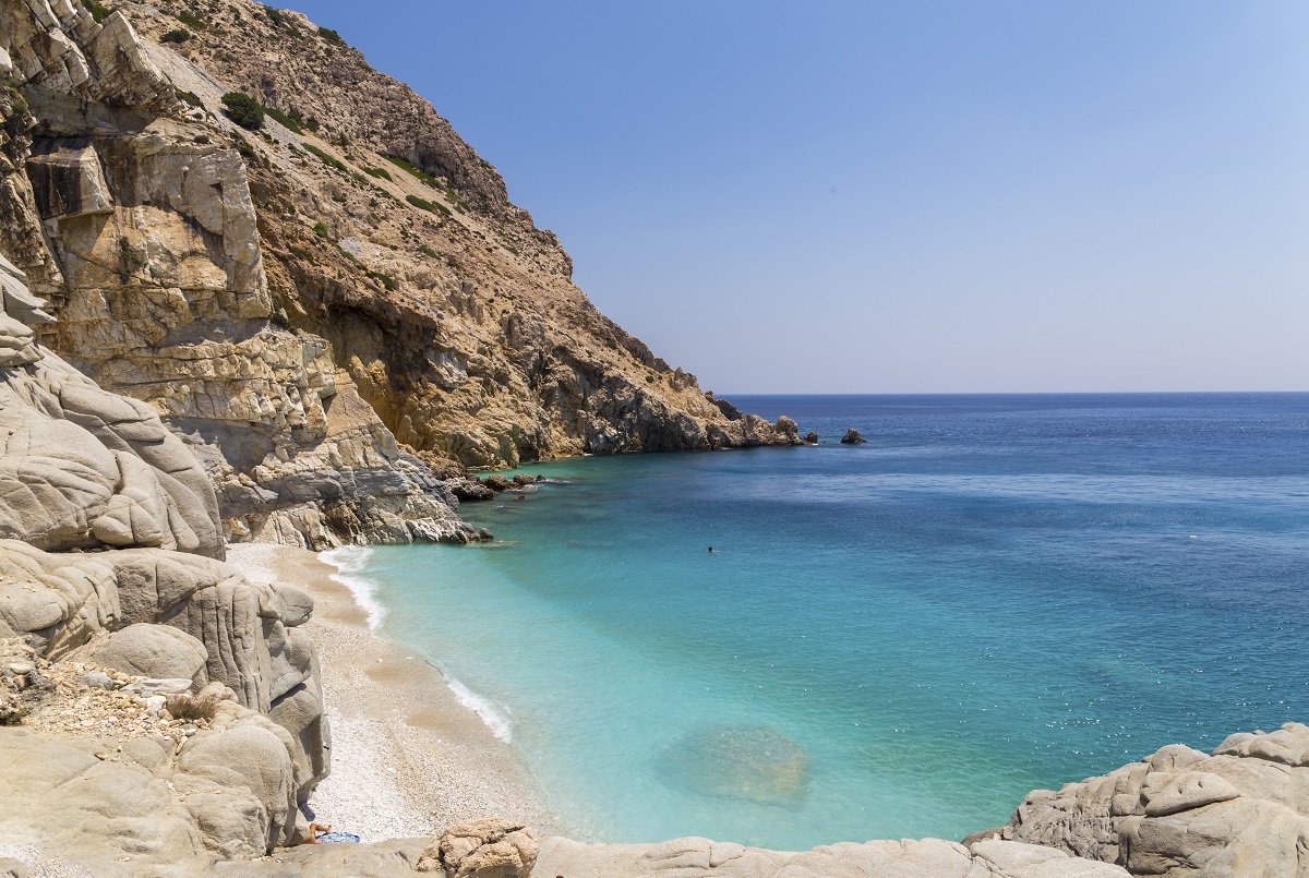 Peisaj care surprinde marea calmă, plaja și stâncile de pe insula Ikaria din Grecia