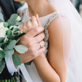 O mireasă, ținută în brațe de soțul ei, cu verighetele la vedere