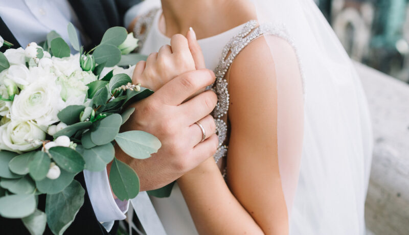 O mireasă, ținută în brațe de soțul ei, cu verighetele la vedere