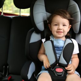 Un băiețel, zâmbește, în timp ce stă într-un scaun auto pentru copii