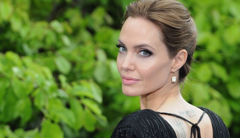 Portret cu Angelina Jolie în timp ce stă cu spatele la cameră și întoarce capul zâmbind la o recepție privată susținută de Disney la Palatul Kensington în mai 2014