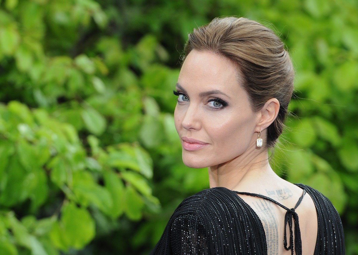 Portret cu Angelina Jolie în timp ce stă cu spatele la cameră și întoarce capul zâmbind la o recepție privată susținută de Disney la Palatul Kensington în mai 2014