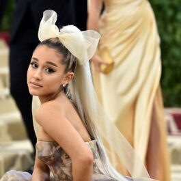 Ariana Grande pe covorul roșu purtând o rochie cu voal galbenă și o fundă mare în păr, la gala Heavenly Bodies din 2018
