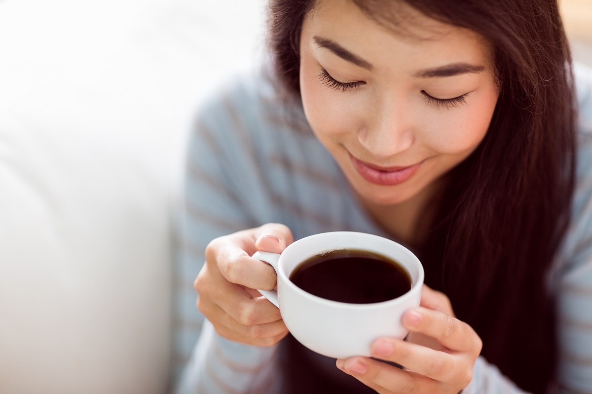 O tânără care ține în mână o cească albă de cafea după ce a aflat când e recomandat să bei cafea