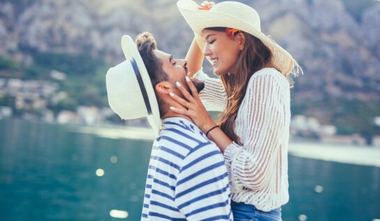 Un cuplu care se ține în brațe în timp ce se sărută și poartă pălării de soare