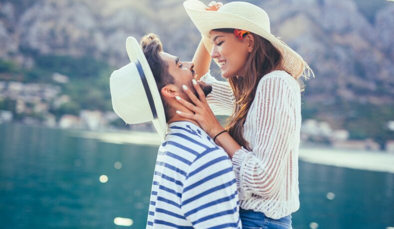 Un cuplu care se ține în brațe în timp ce se sărută și poartă pălării de soare