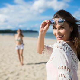 O femeie frumoasă, îmbrăcată în alb, își ridică ochelarii de soare, în timp ce se află pe plajă