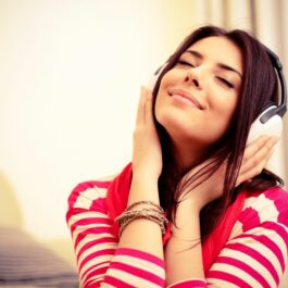 O tânără surânde, cu ochii închiși, în timp ce ascultă muzică la cășți