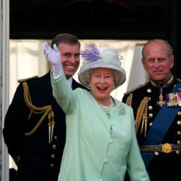 Regina Elisabeta îmbrăcată în costum verde în timp ce face cu mâna publicului de la balcon alături de Prințul Philip și alte figuri din corpul Regal la ceremonia oficială a comemorării zilei naționale în iulie 2005