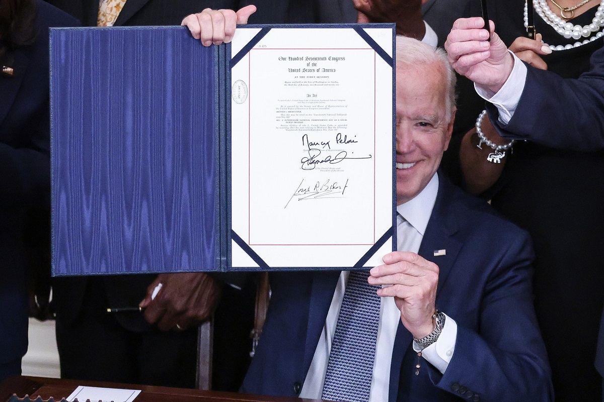 Președintele Joe Biden în timp ce ține în mână actul care stabilește că Juneteenth va fi zi de sărbătoare națională