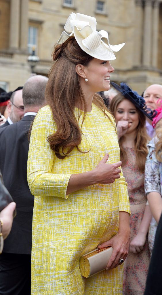 Ducesa Kate Middleton într-o rochie galbenă în timp ce salută publicul și este însărcinată cu primul copil la o vizită oficială găzduită de Regina Elisabeta în mai 2013
