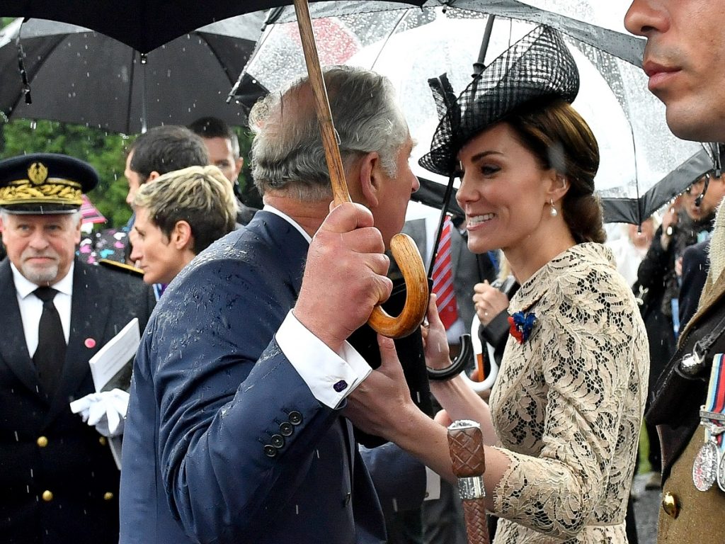Ducesa Kate Middleton într-o rochie albă în timp ce se uită la Prințul Charles care ține o umbrelă la comemorarea centenarului din 2016 al bătăliei Somme