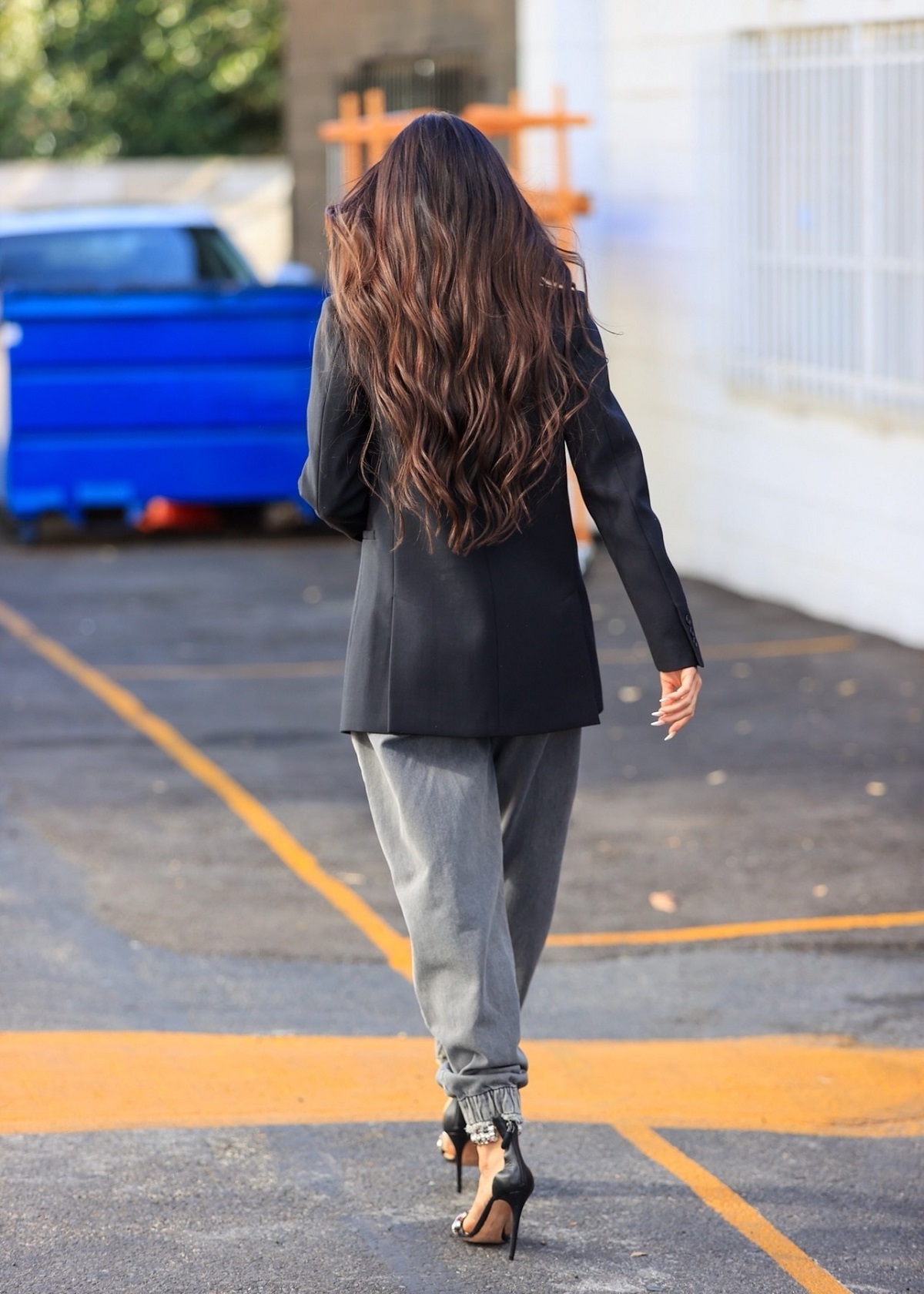 Megan Fox cu spatele în timp ce poartă un sacou negru, o pereche de blugi gri și tocuri negre