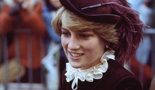 Portret cu Lady Di în timp ce zâmbește oamenilor și poartă o cămasă violet cu guler bufant alb, la care a accesorizat o pălărie mov, într-unul din acele momente emblematice ale Prințesei Diana