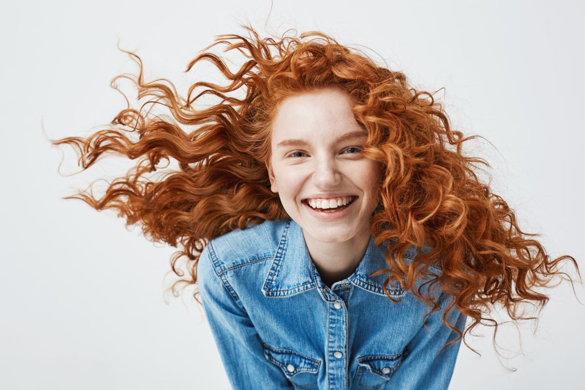 Portretul unei tinere roșcate, zâmbitoare și cu buclele în vânt
