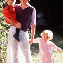 Lady Di într-o fustă cu buline și o vestă mov în timp ce ține o fetiță de mână și a alta în brațe în timp ce lucra la o școală de asistente în 1980, fiind unul dintre acele momente emblematice ale Prințesei Diana