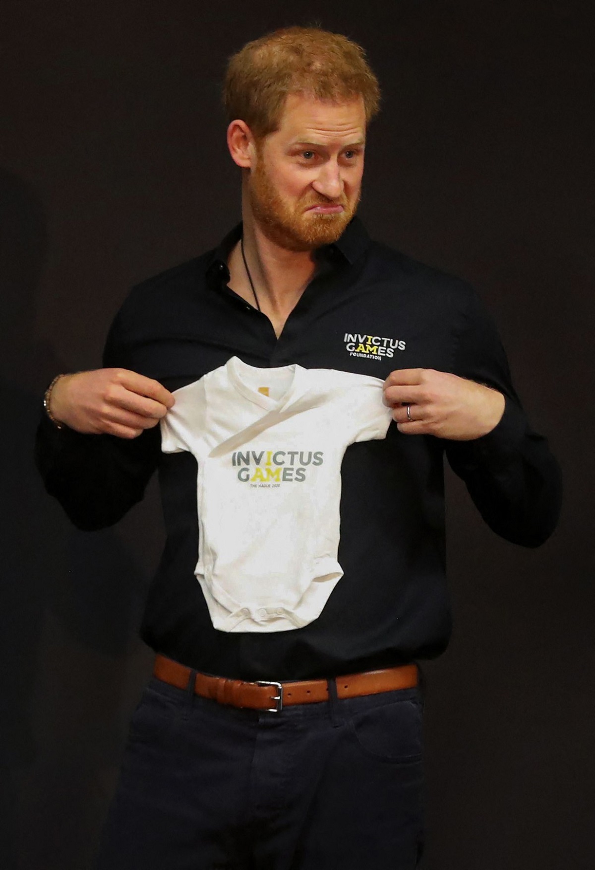 Prințul Harry ținân în mână un body de bebeluș la prezentarea Jocurilor Invictus la Haga în 2019