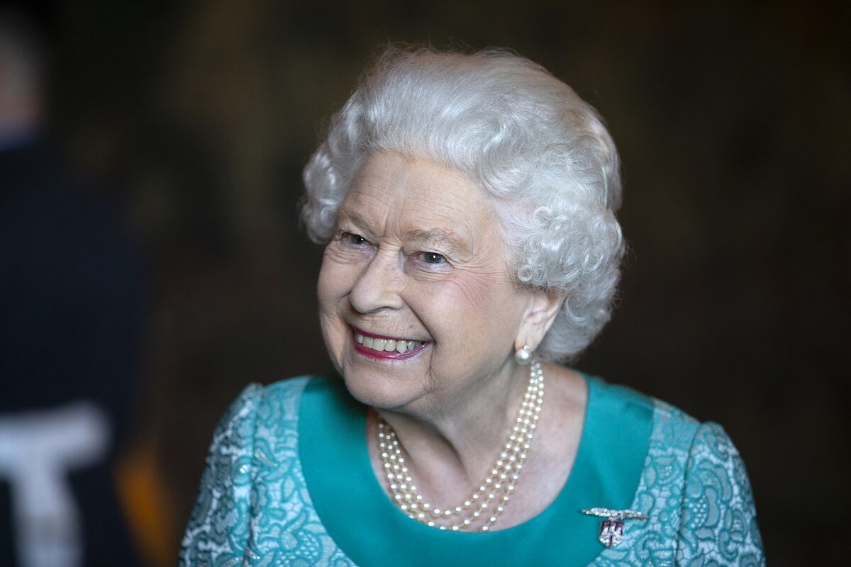 Portret al Reginei elisabeta îmbrăcată într-o rochie albastră în timp ce zâmbește la o recepție oficială din 2018 de la palatul din Edinburgh, Holyroodhouse