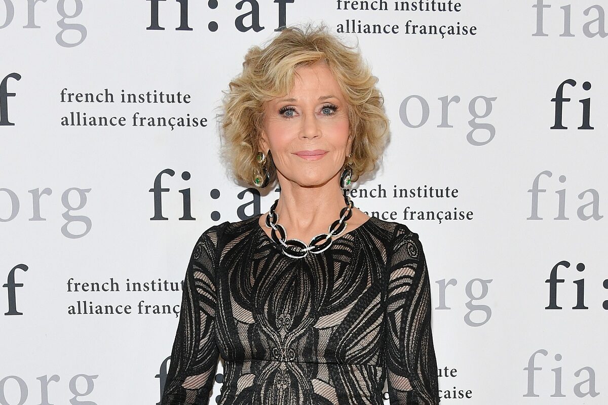 Portret al actriței Jane Fonda îmbrăcată într-o rochie neagră în timp ce zâmbește la camere și stă în spatele unui panou publicitar la Gala Trophee des Arts din New York din 2018
