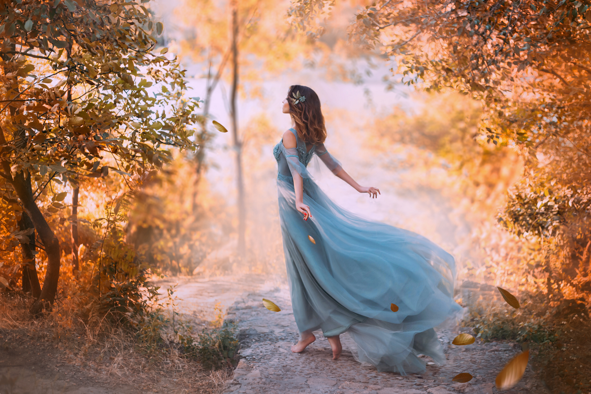 O femeie frumoasă care stă cu spatele într-o pădure și poartă o rochie albastră în timp ce o briză o ridică pentru a reprezenta zodiile de aer