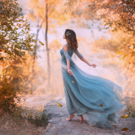 O femeie frumoasă care stă cu spatele într-o pădure și poartă o rochie albastră în timp ce o briză o ridică pentru a reprezenta zodiile de aer