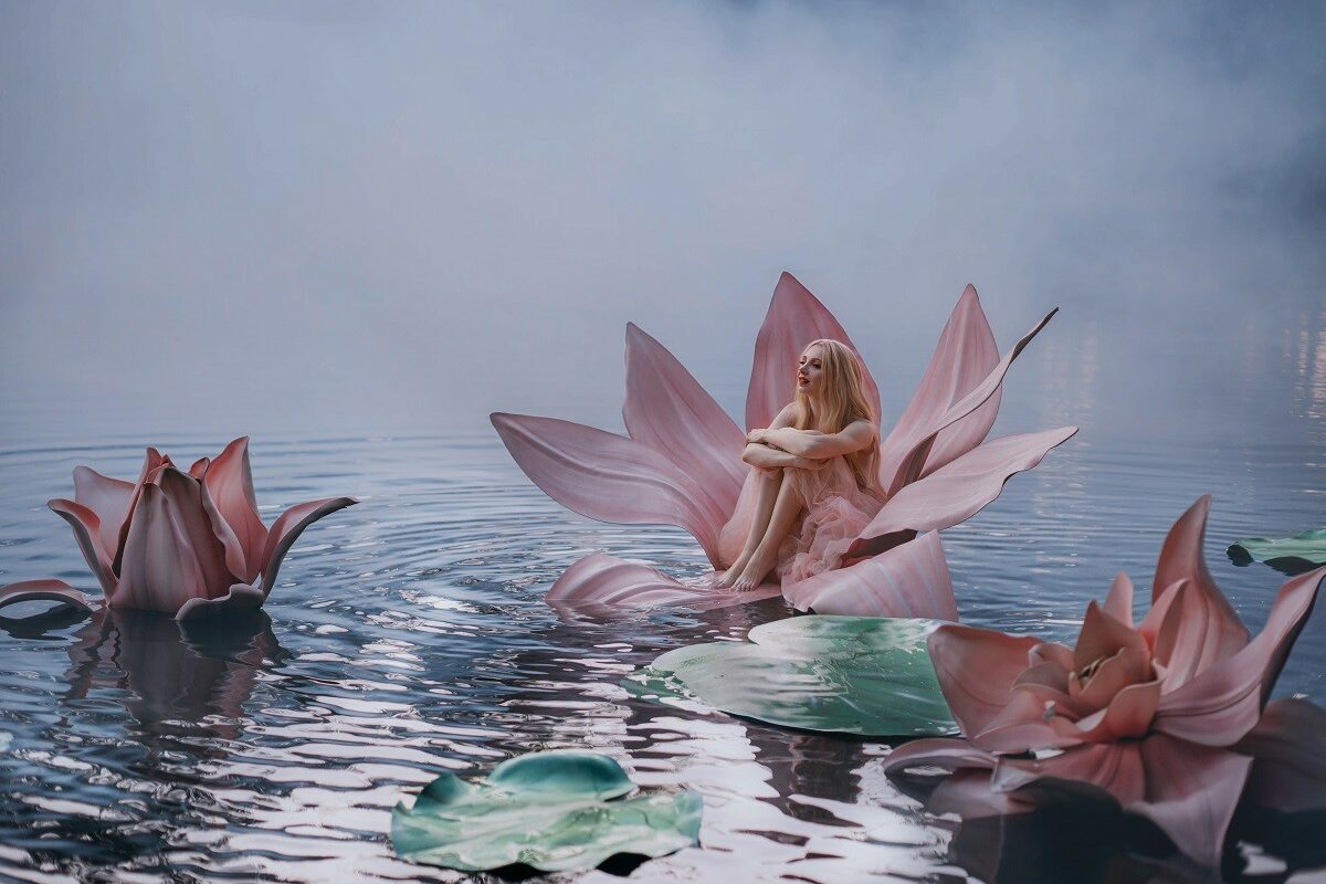 Un lac liniștit învăluit de ceață pe care se află trei flori roz de nufăr, iar în interiorul acestora stă o femeie frumoasă care reprezintă zodiile de apă și liniștea acestora