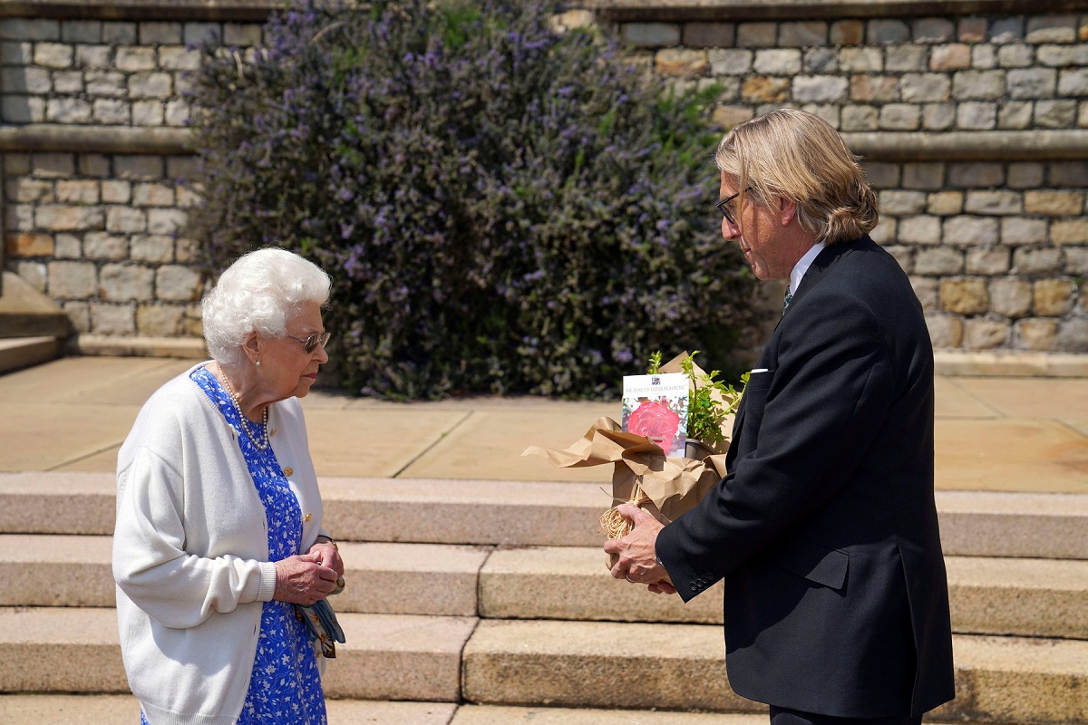 Regina Elisabeta în rochie albastră și jachetă albî alături de președintele Societății Regale de Horticultură Keith Weed care e îmbrăcat la costum și ține în mâini un trandafir