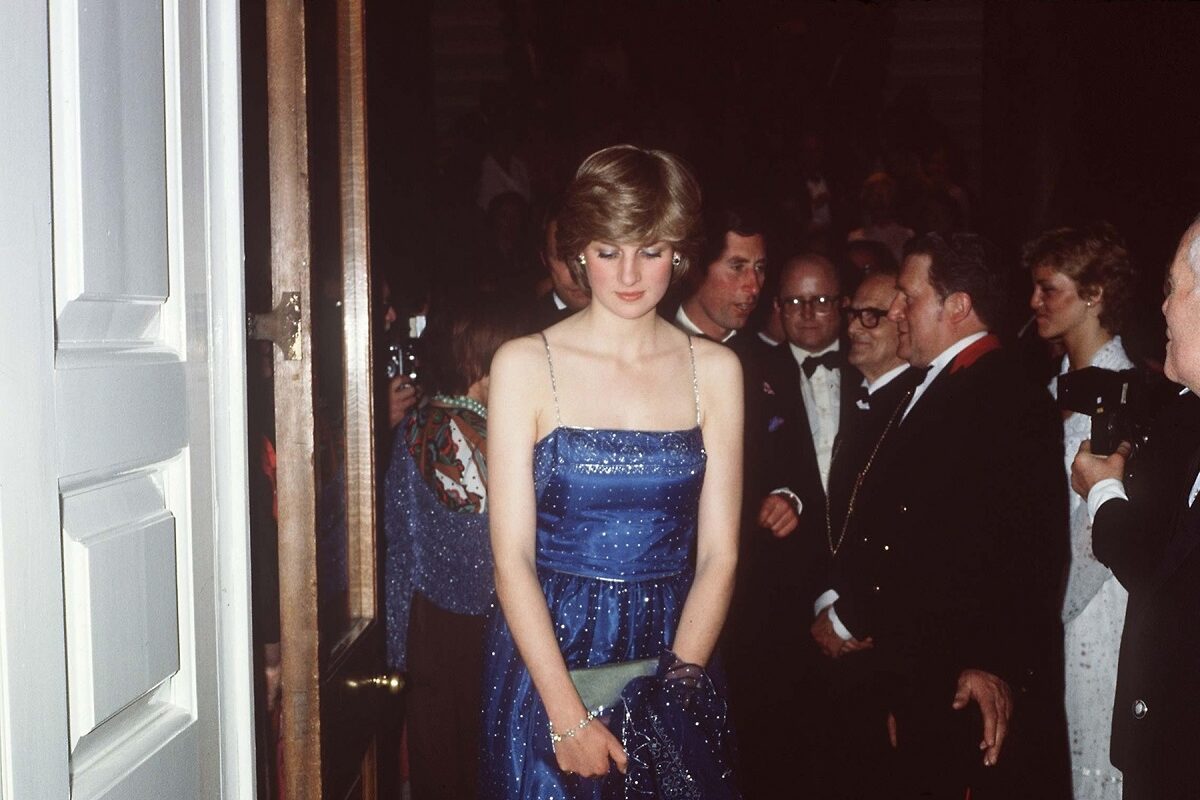 Prințesa Diana purtând o rochie albastră cu paiete în timp ce pășește afară dintr-o încăpere de la un eveniment oficial