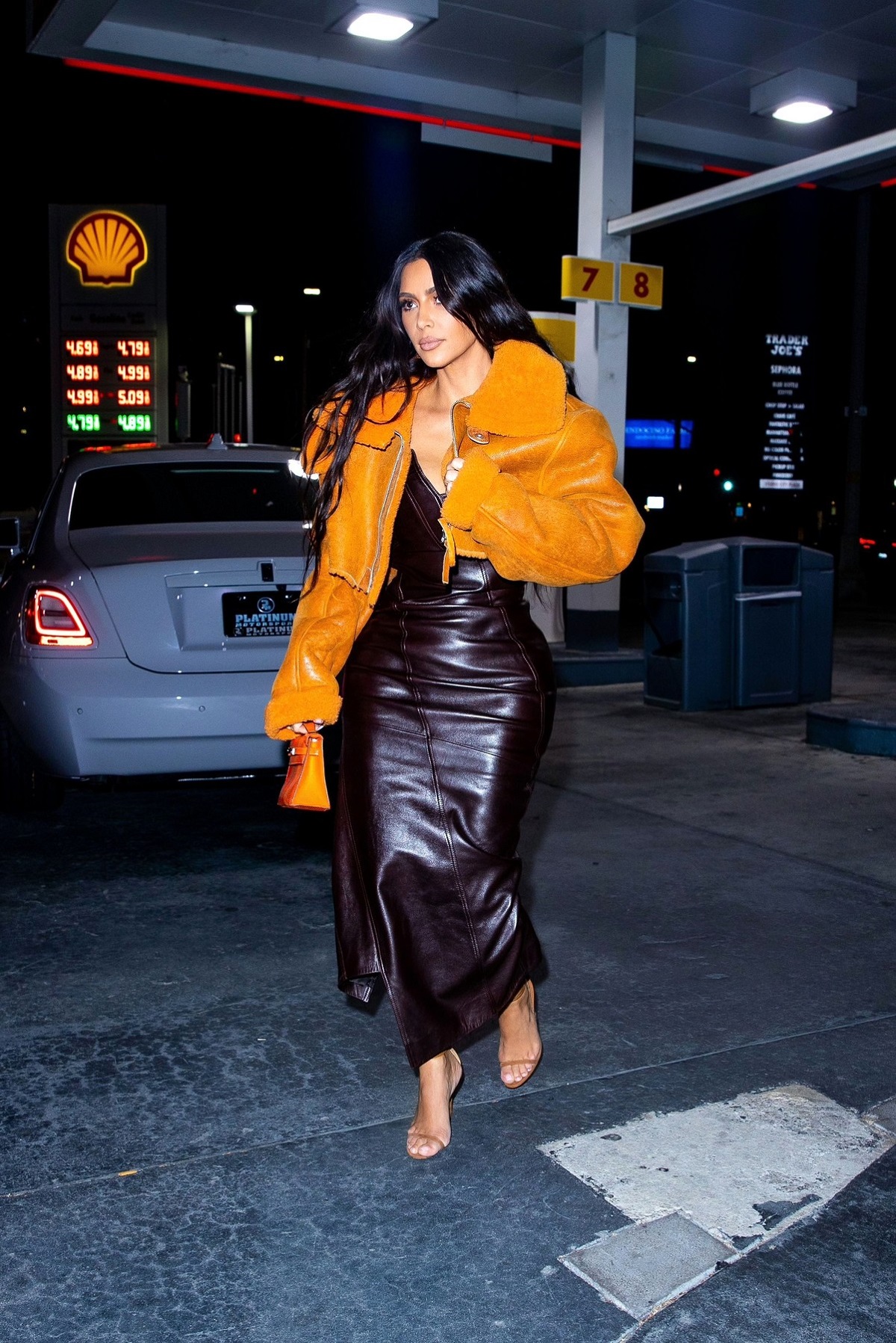 Kim Kardashian într-o parcare din Los Angeles purtând o rochie de piele neagră și o jachetă orange de la un drand deținut de Kanye West