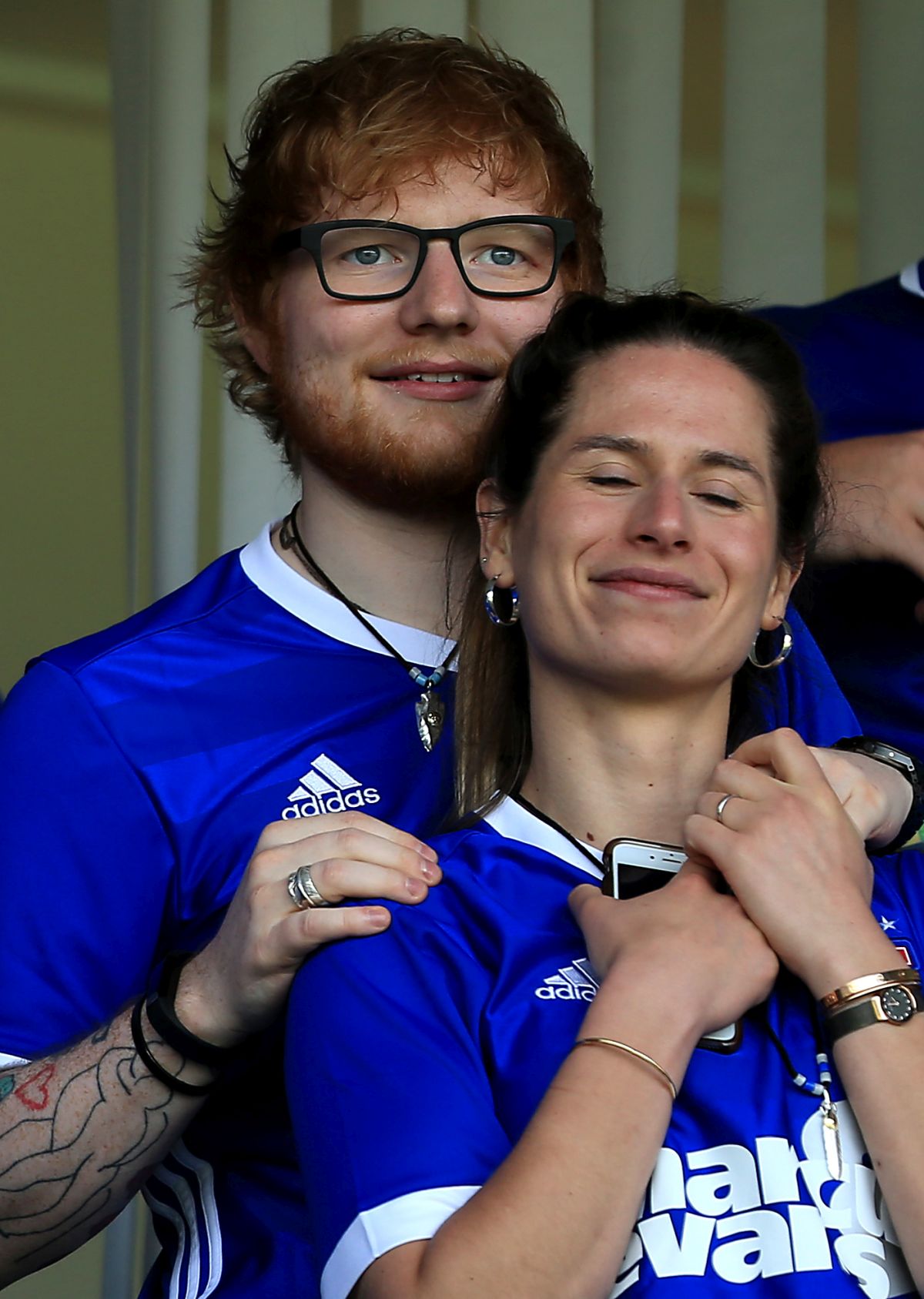Ed Sheeran și soția sa, îmbrăcați în tricouri albastre, cu alb, la un meci de fotbal