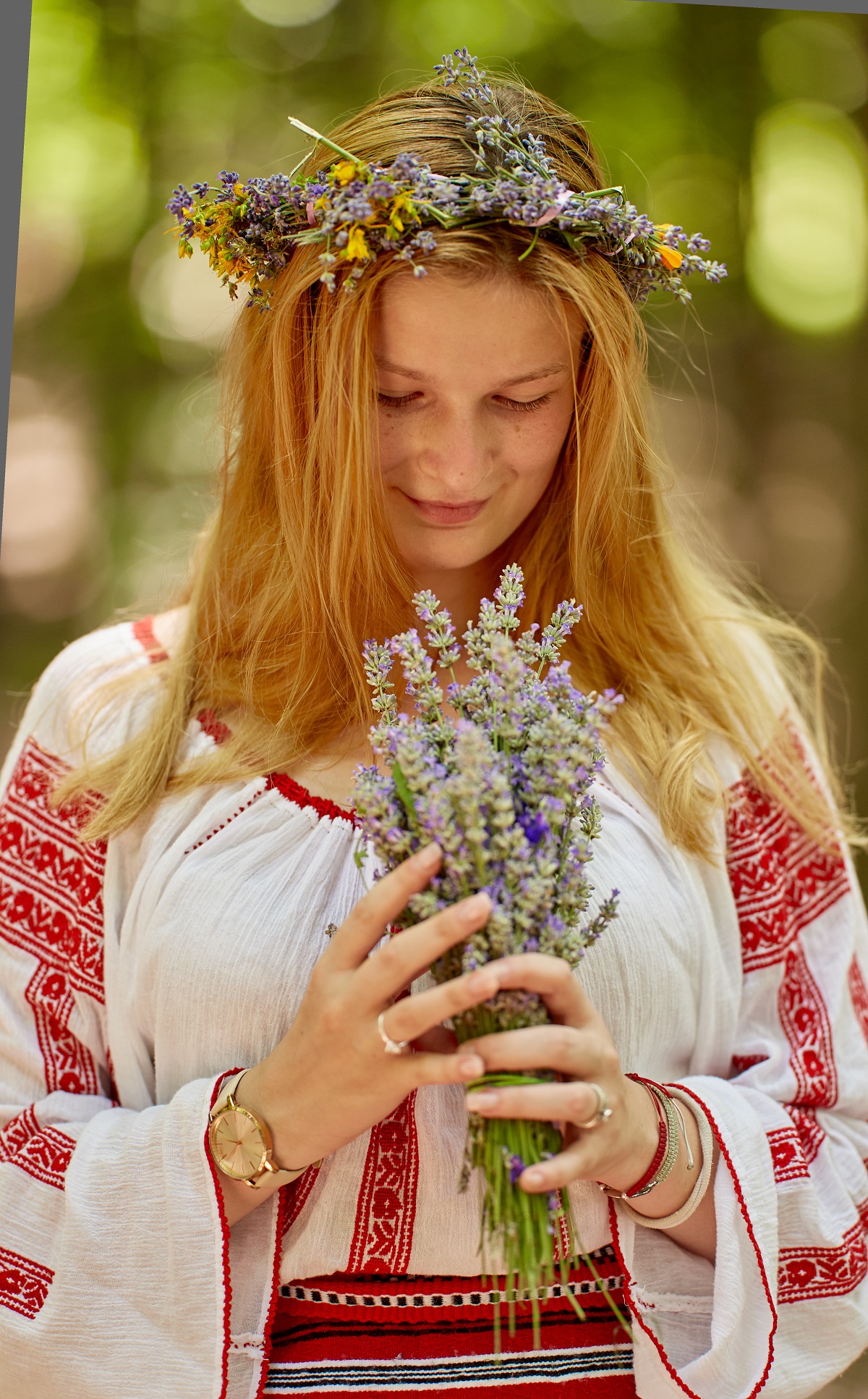 O femeie frumoasă blondă îmbrăcataă în prot tradițional românesc în timp ce ține în mână un buchet de lavandă