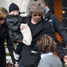 Brad Pitt, cu sacou și pălărie, își poartă fiul în brațe
