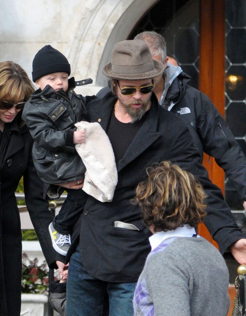 Brad Pitt, cu sacou și pălărie, își poartă fiul în brațe