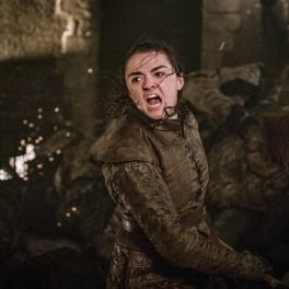 Maisie Williams în rolul lui Arya Stark, Game of Thrones, în timpul unei bătălii din sezonul 8, fundal maro și închis
