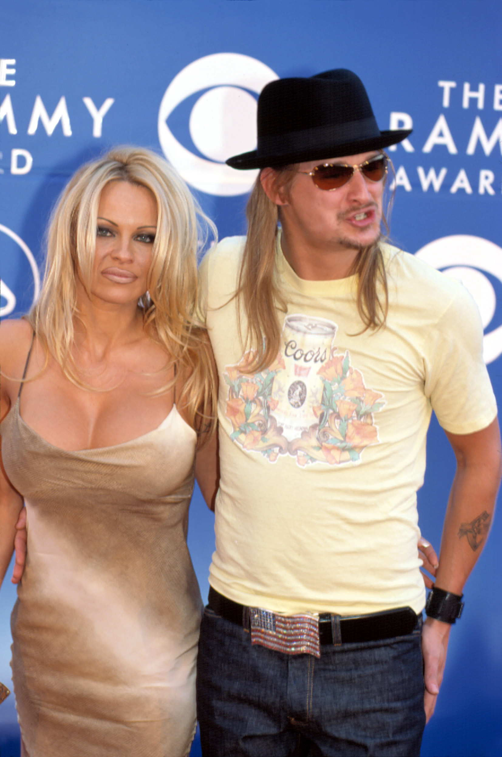 Pamela Anderson și Kid Rock la Premiile Grammy din 2002, covorul rosu, ea in rochie aurie mulata, el in tricou galben, palarie neagra
