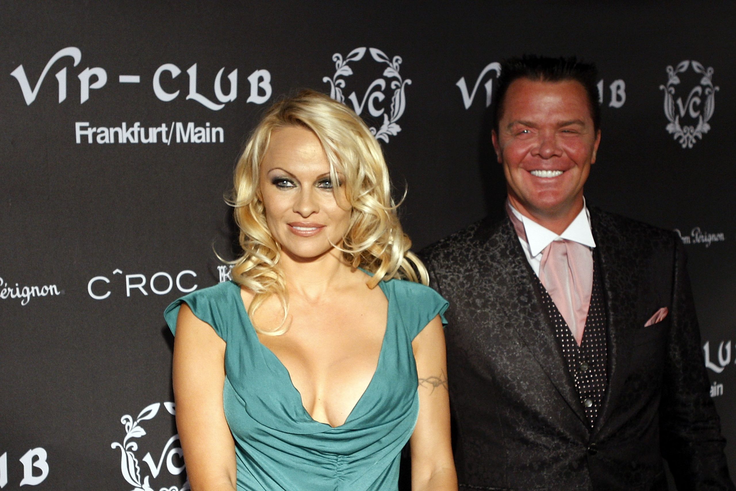 Pamela Anderson la deschiderea clubului VIP din Germania, 2009, covor rosu, fundal negru, ea poarta o bluza albastra cu decolteu