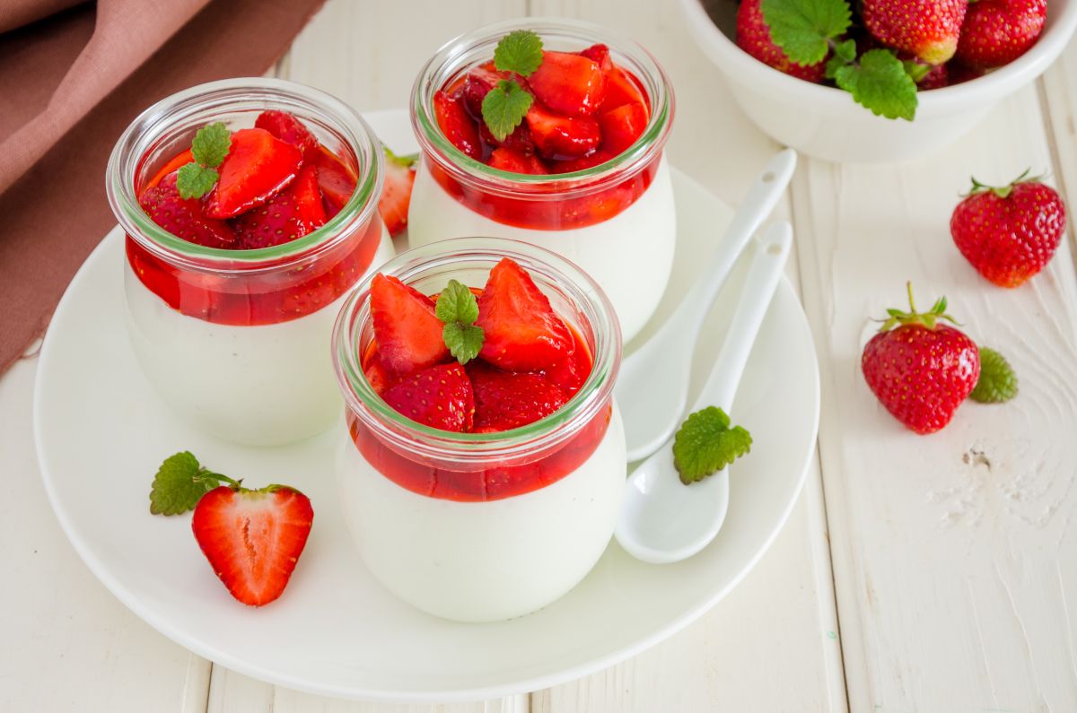 Trei pahare care conțin panna cotta cu vanilie și sos de căpșuni, decorate cu căpșuni întregi.