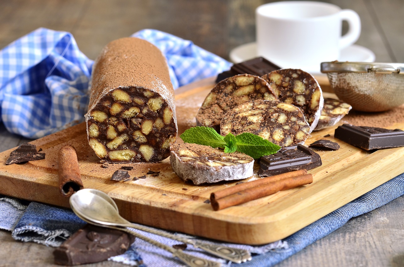 Salam de biscuiți cu ciocolată decorat cu pudră de cacao, pe un suport de lemn