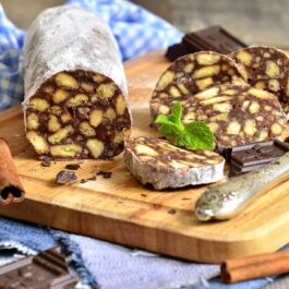 Salam de biscuiți cu ciocolată decorat cu zahăr pudră, pe un suport de lemn
