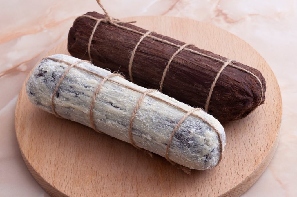 Salam de biscuiți cu ciocolată decorat cu pudră de cacao și cu zahăr, pe un suport de lemn