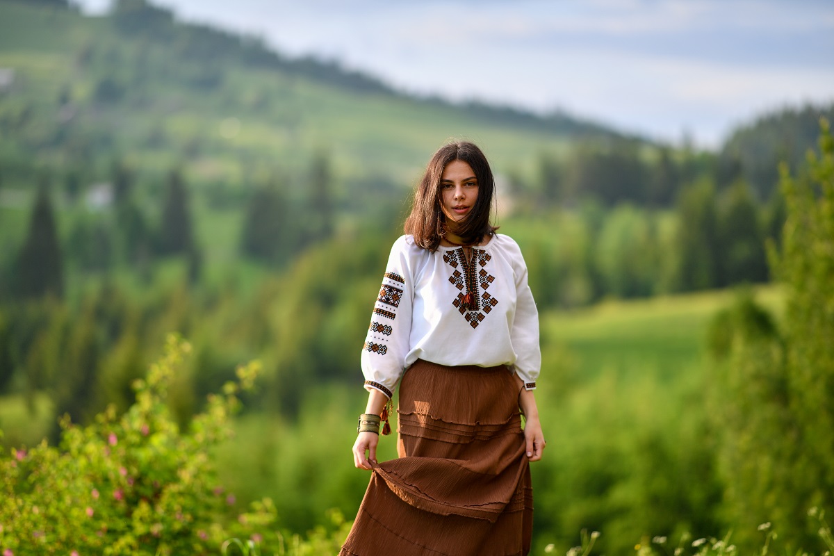 O tânără frumoasă purtând un costum tradițional românesc în timp ce se află pe o pajiște verde