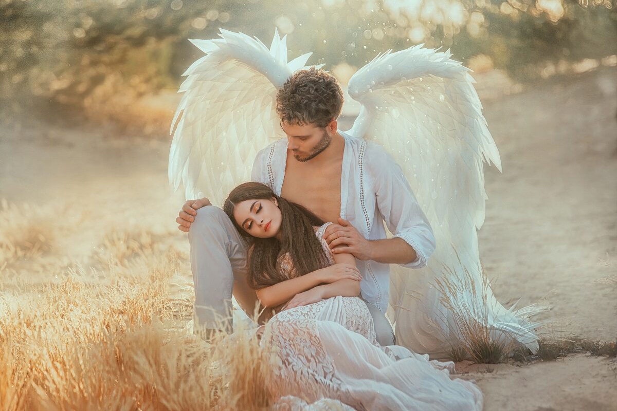 Unul din bărbații care fac femeile cu adevărat fericite, având aripi de înger și stând în genunchi în timp ce o ține după umeri pe iubita sa frumoasă care poartă o rochie albă diafană